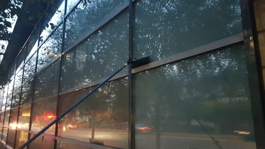 A person cleaning a large glass window on a building as morning sets in.